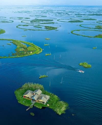 Open water and long green phumdi banks on Loktak Lake, a boat crossing in the distance
