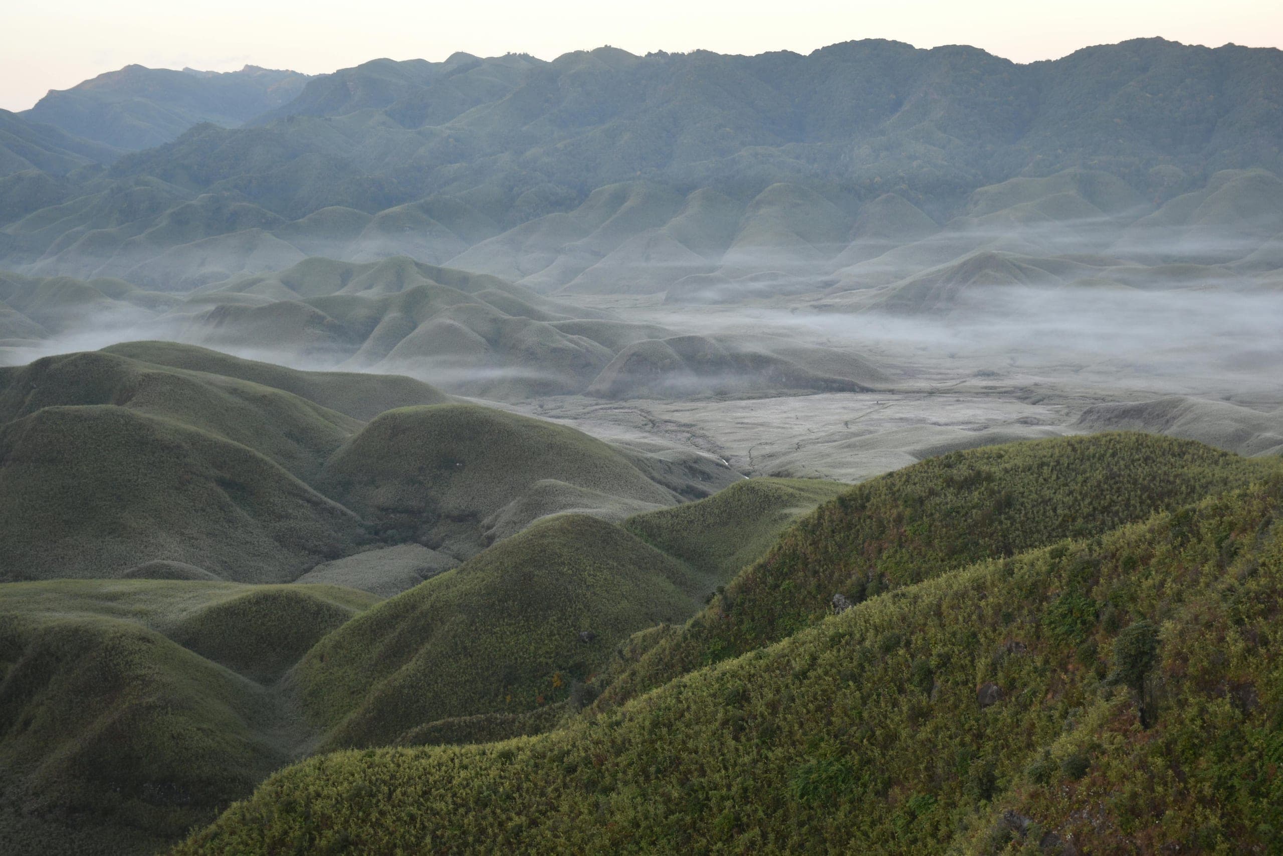 Rolling green hills layered into the distance with mist settling in the valleys between them at first light