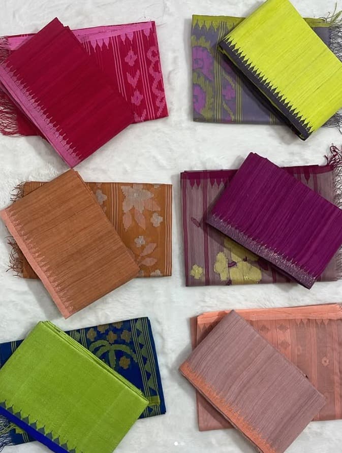 Folded lengths of Manipuri phanek cloth in magenta, lime, orange and purple, each edged with a woven temple-point border